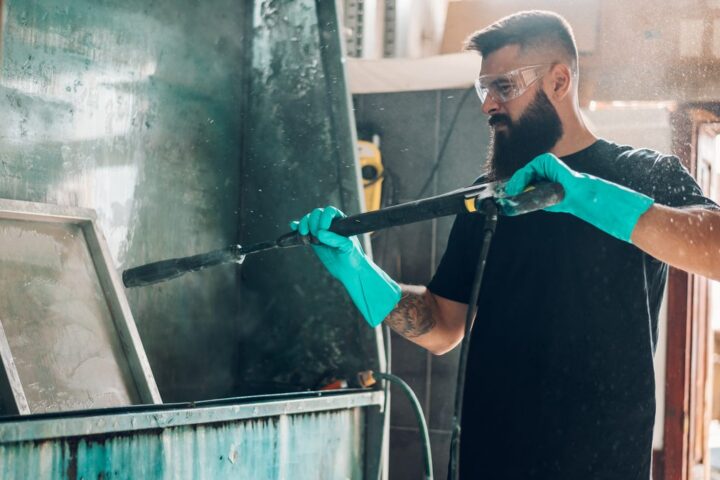 Ilustrační stock: pracovník v dílně drží pistoli na stlačený vzduch u rozvodu kompresoru, ofukuje stroj, má ochranné brýle