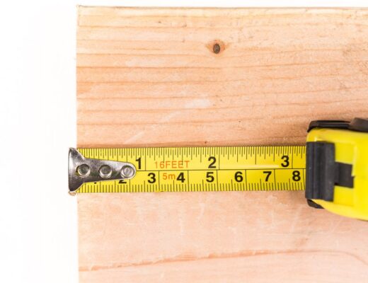 Ilustrační stock: svinovací metr s kovovým háčkem na konci pásku, detail posuvného uchycení nýtky, dílna nebo pracovní stůl s prknem, civilně, bez loga